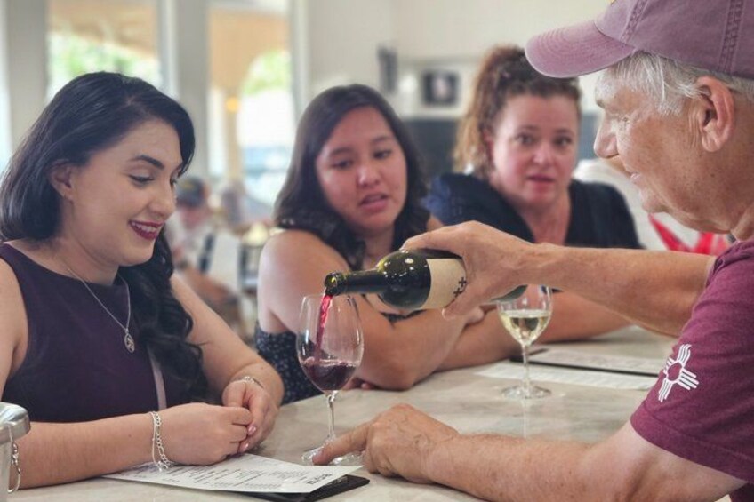 A person pouring wine into a glass at a table with other people seated around. 4