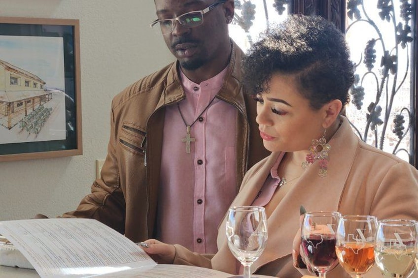 A man and a woman sitting at a table with documents and glasses of wine. 2