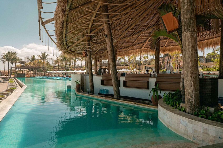 A pool with a thatched roof, palm trees, and lounge chairs. 4