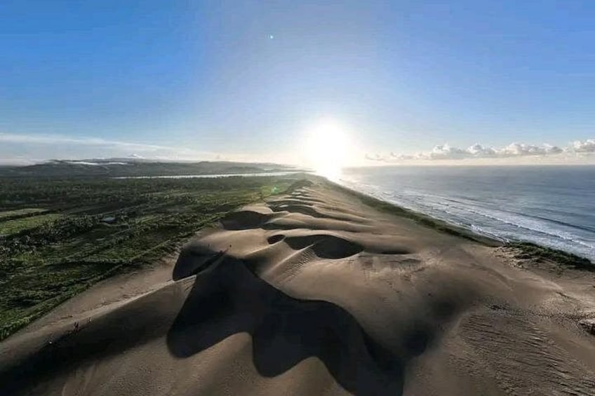 A coastal landscape with sand dunes, a beach, and a distant shoreline. 1