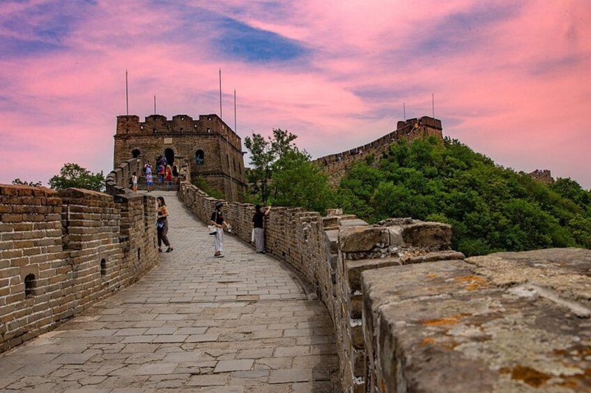 A historical stone wall with a paved walkway, leading to a large brick structure with towers. 2