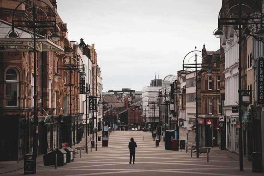 A person standing on a pedestrian crossing in a city with historic buildings and street lamps. 1