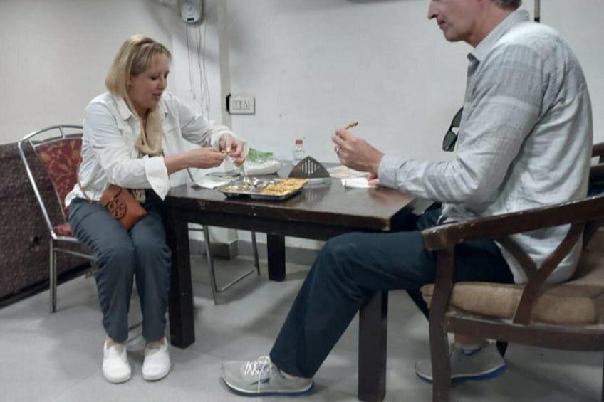 Due persone sedute a tavola con del cibo, una con un piatto in mano e l'altra con una forchetta. 3