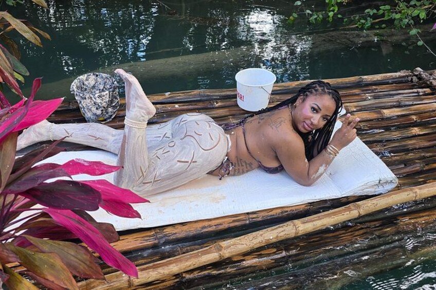 Una persona recostada en un tapete dentro de una barca de bambú sobre el agua, rodeada de plantas. 2