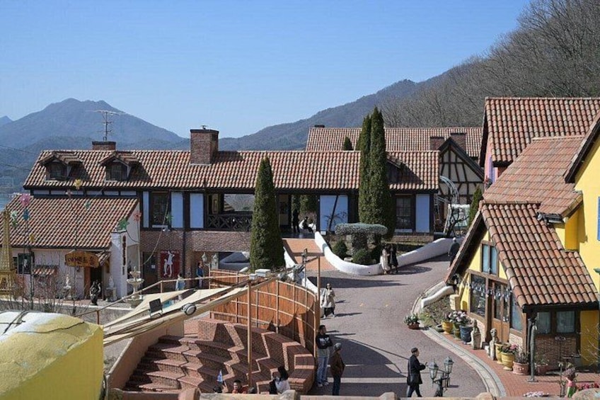 A village with traditional buildings, a winding street, and mountains in the background. 2