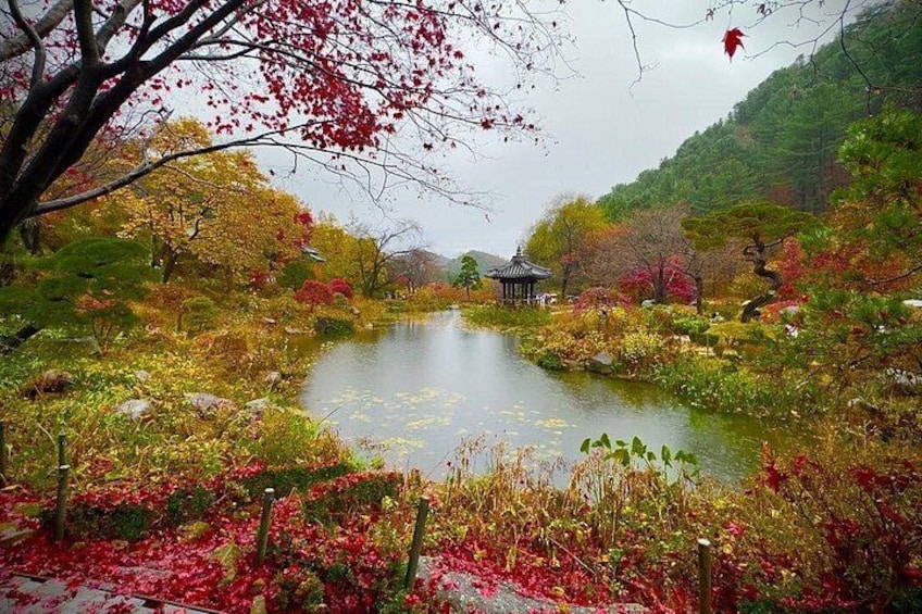 A serene pond surrounded by autumn foliage, a traditional gazebo, and a mountainous backdrop. 4