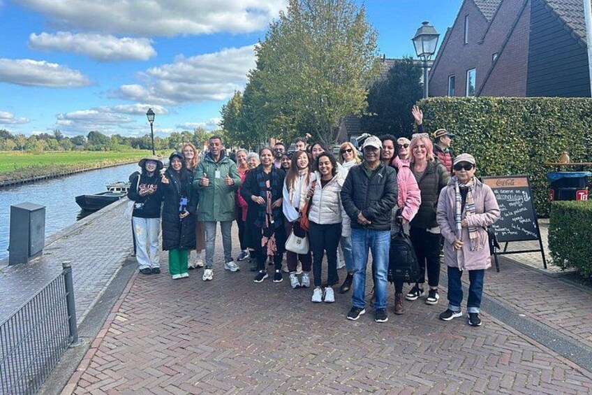 A group of people standing on a brick pathway by a canal, with a building and trees in the background. 4