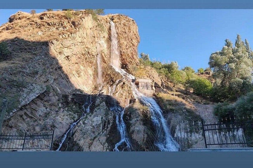 Una cascada se precipita por un acantilado rocoso, rodeada de árboles y una valla. 4
