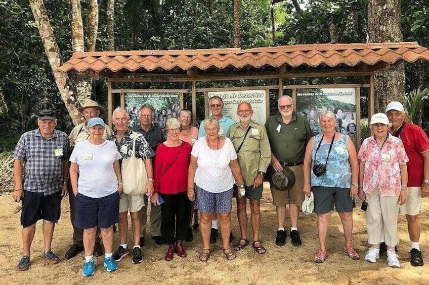 A group of people standing in front of a structure with a tiled roof, surrounded by trees. 3