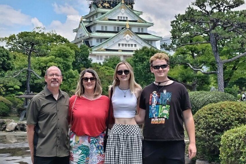 A group of people standing in front of a castle with a pond and trees. 1
