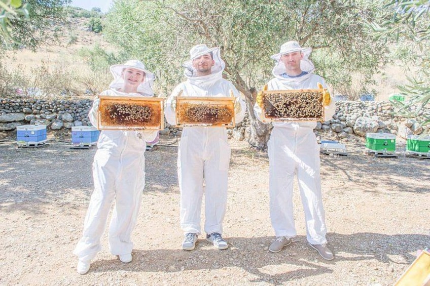 Trois personnes vêtues de combinaisons de protection blanches, tenant des cadres de ruche. 2