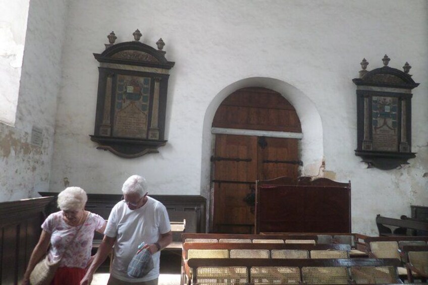 Interior de una iglesia antigua con bancos de madera, una gran puerta de madera y dos relojes en la pared. 5