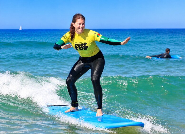 A person surfing on a blue board with a yellow shirt and black wetsuit. 2