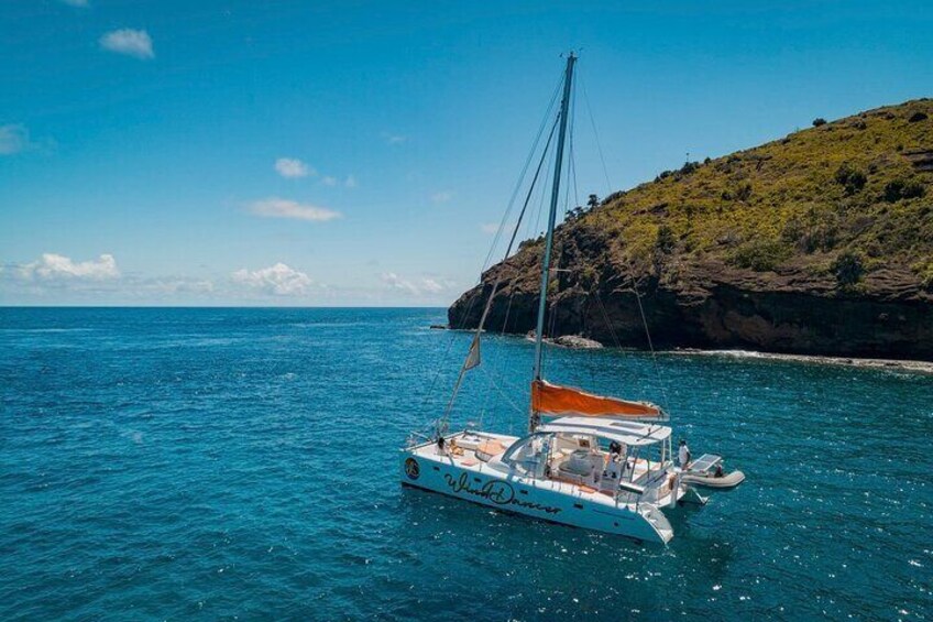 A white catamaran with an orange canopy sailing on turquoise waters near a rocky coastline. 1