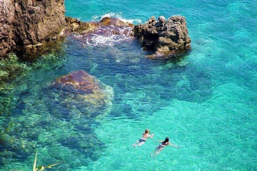 Three people swimming in clear turquoise water near rocky formations. 5