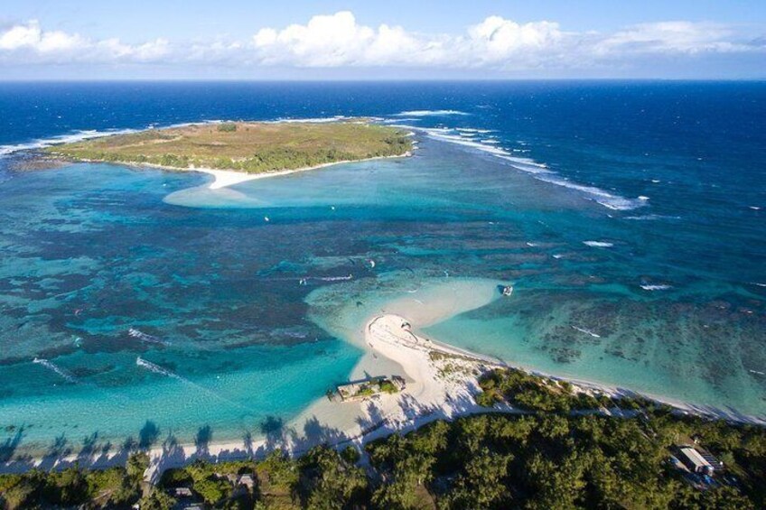An aerial view of a coastal area with clear turquoise waters, a sandy beach, and a small island with vegetation. 1