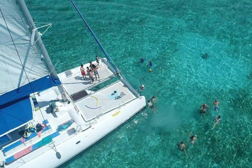 A sailboat with people swimming in clear turquoise water. 3