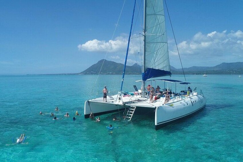 Un'imbarcazione a vela con persone che nuotano in acqua e un paesaggio montuoso sullo sfondo. 1