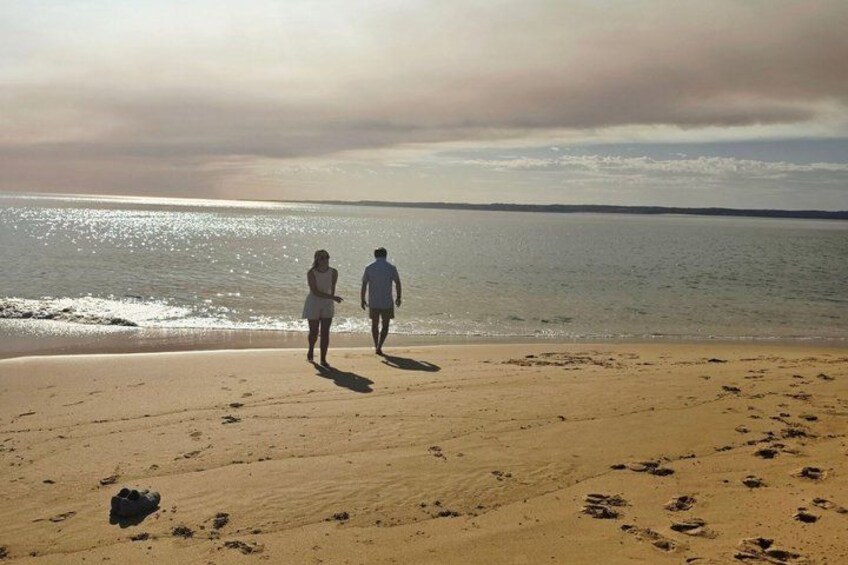 Una playa con huellas y una pareja caminando hacia el agua. 3