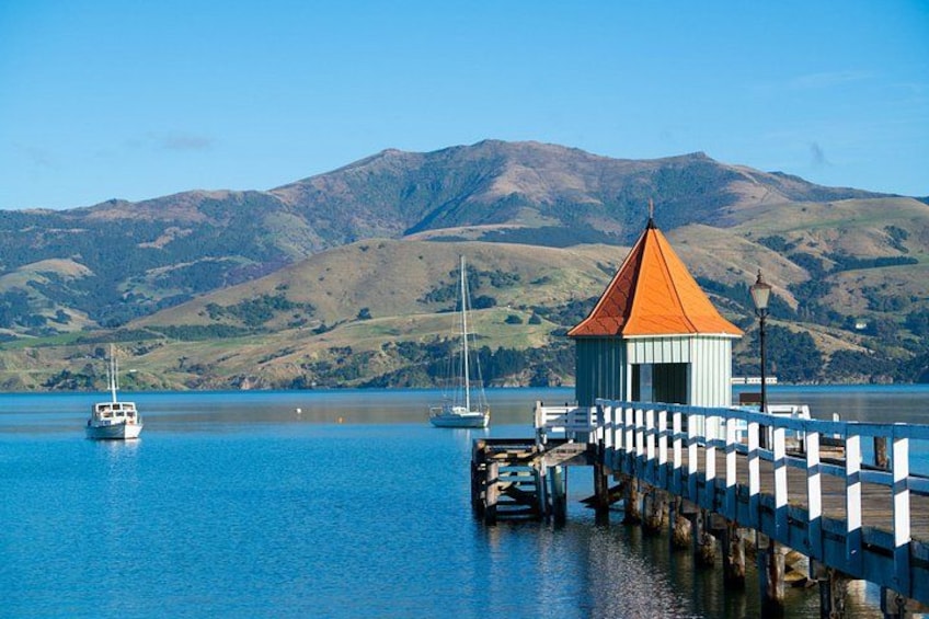 A coastal scene with a wooden pier, a small building with a red roof, and sailboats on calm waters. 4