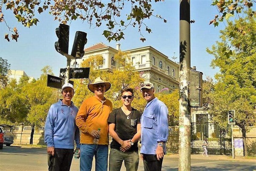 Cuatro personas de pie frente a un semáforo, con un edificio al fondo. 1