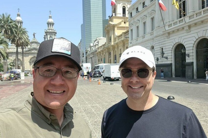 Dos personas de pie frente a un edificio histórico con columnas y una torre del reloj. 4