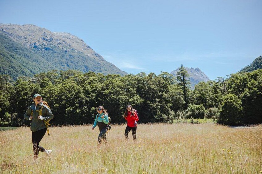Three people hiking in a grassy field with mountains in the background. 3