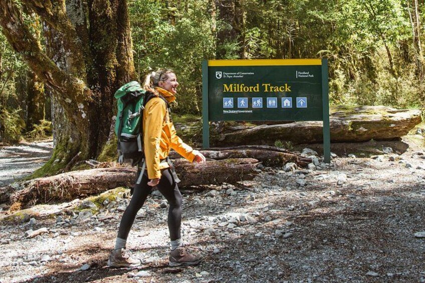 A hiker on the Milford Track with a sign indicating the trail and its features. 1