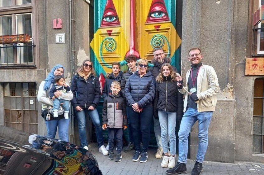 En gruppe mennesker står foran en farverig mural med geometriske mønstre og øjne. 5