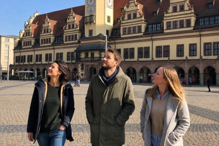 Tre personer står i en firkantet plads med historiske bygninger i baggrunden. 1