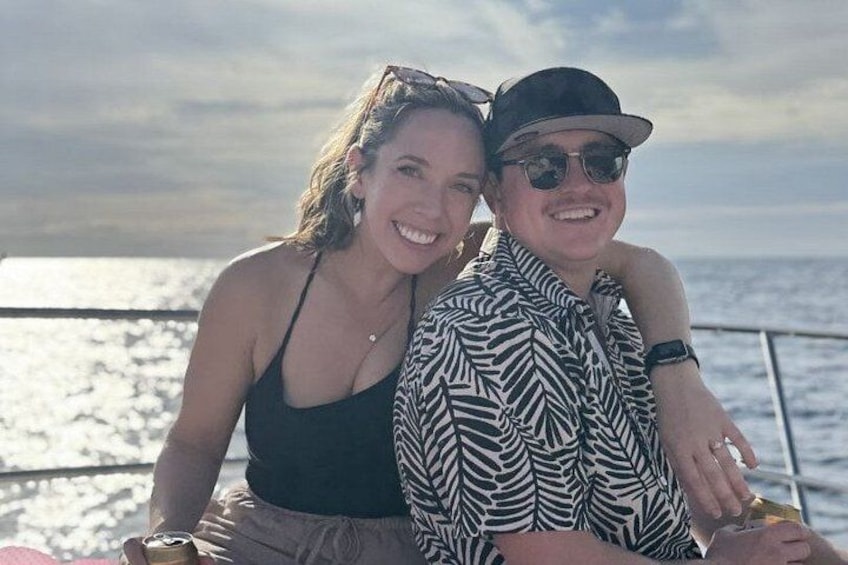 Two people sitting on a boat with a body of water and a cloudy sky in the background. 1