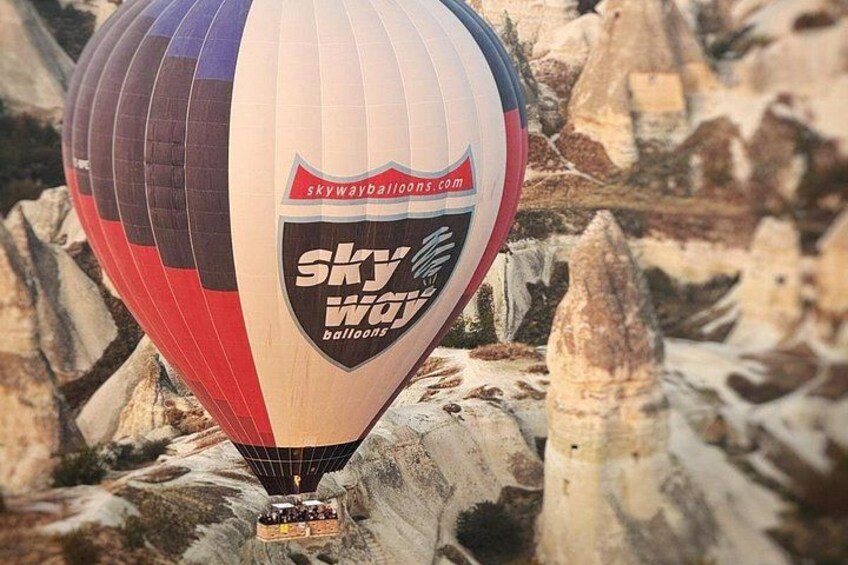 Een luchtballon met een logo, die boven een rotsachtig landschap zweeft. 3
