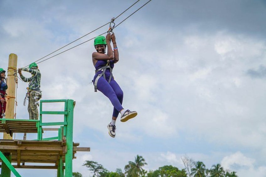 A person zip-lining with safety harnesses, a wooden platform, and palm trees in the background. 5