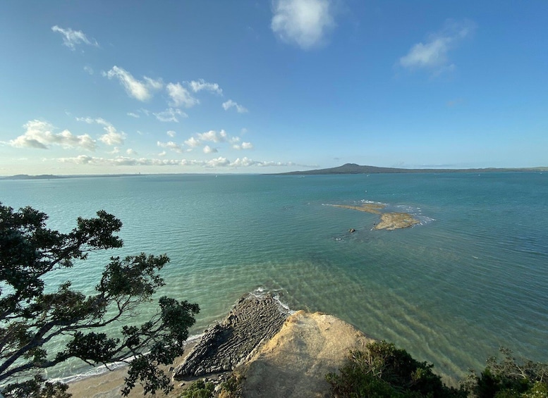 A coastal landscape with clear blue waters, a sandy beach, and rocky outcrops. 1