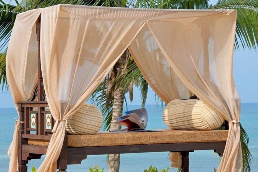 A beach cabana with a canopy, cushions, and a small table. 4