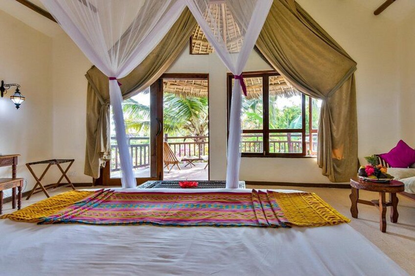 A bedroom with a bed, curtains, a table, and a view of the outdoors. 5