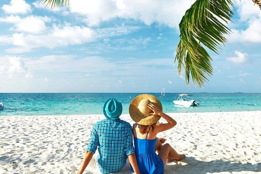 Two people sitting on a beach with a boat in the background. 1