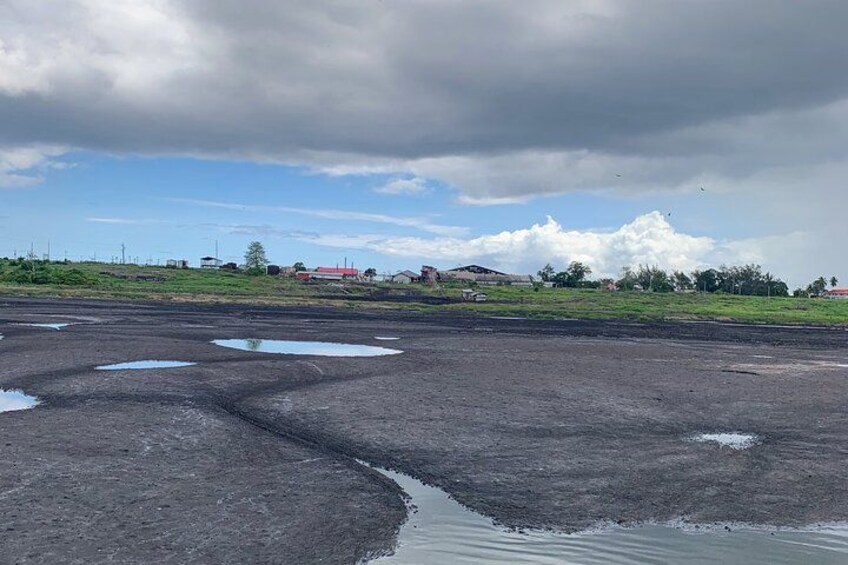 Une chaussée en asphalte mouillée, parsemée de flaques d’eau, un ciel nuageux et des bâtiments qui se dessinent à l’horizon. 2