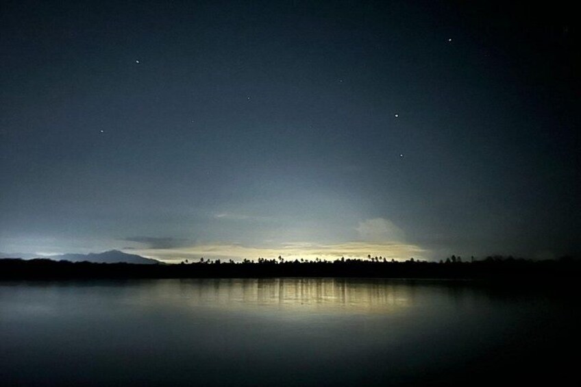 A calm lake at night with a mountain silhouette in the background and a few stars visible in the sky. 3