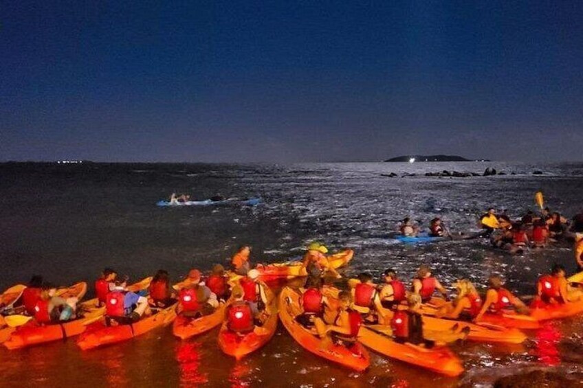 A nighttime kayaking activity with participants in orange kayaks on a beach. 2