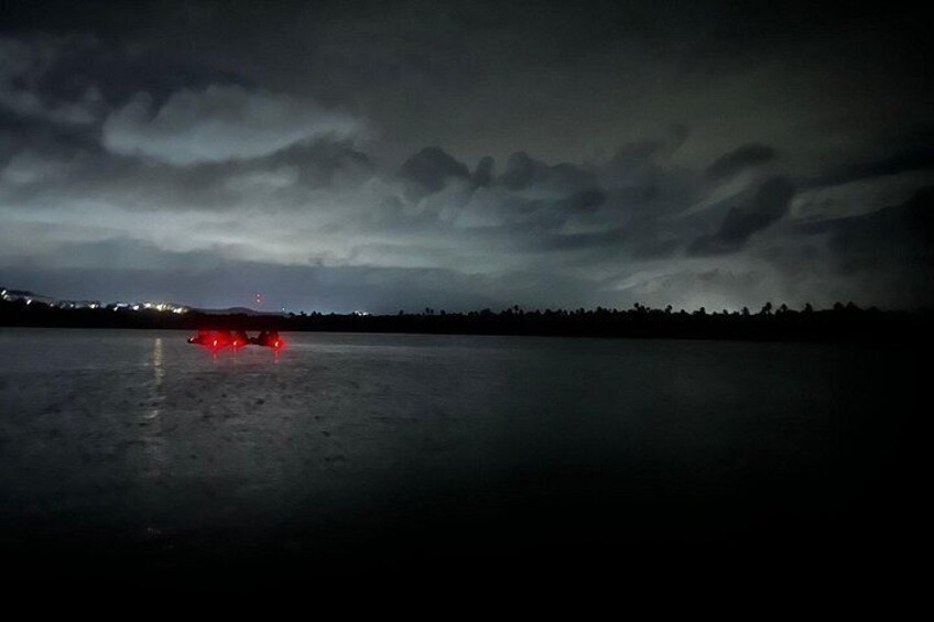 A nighttime scene with a body of water reflecting lights, a cloudy sky, and a distant shoreline with lights. 4