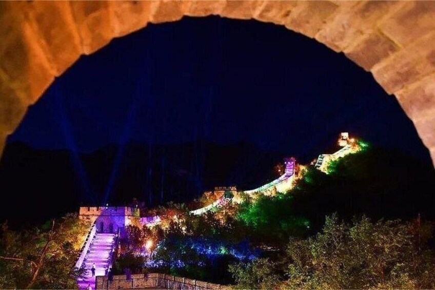 A brightly lit bridge under an arched stone structure at night. 2