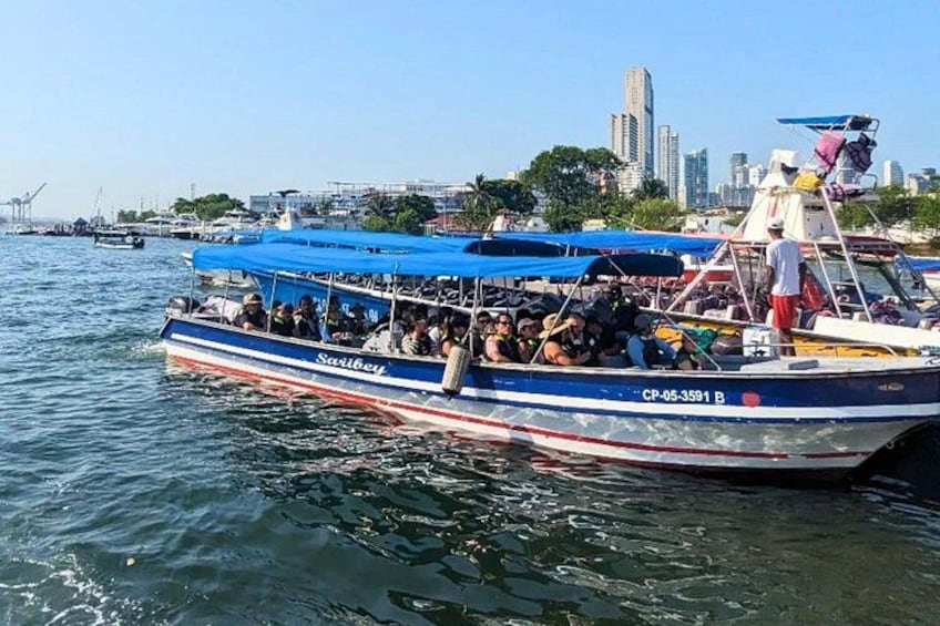 A boat with passengers, a city skyline in the background, and water. 2