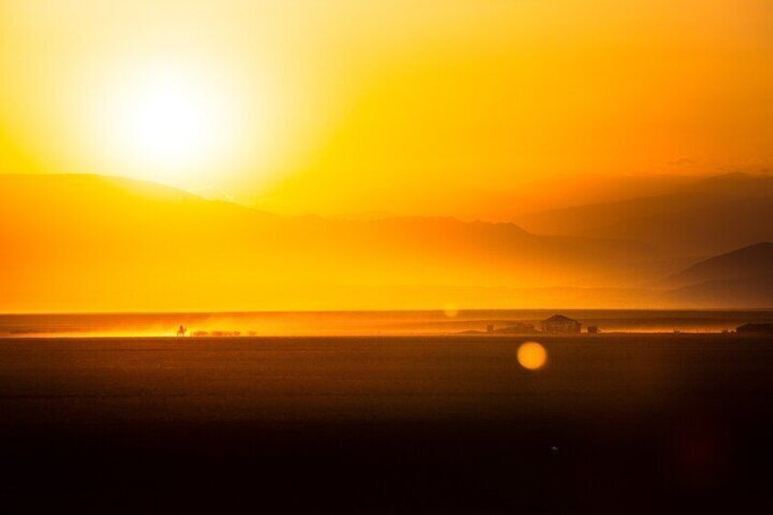 A sunset over a flat landscape with a few structures in the distance. 3
