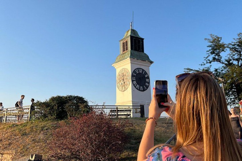 A clock tower with a green roof, surrounded by a fence and greenery. 1