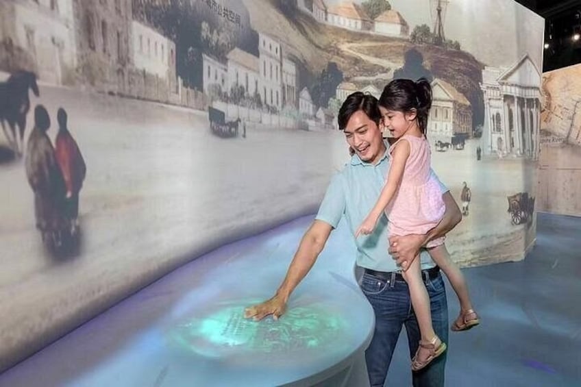 Un uomo e un bambino davanti a un murale storico con un display digitale interattivo. 4