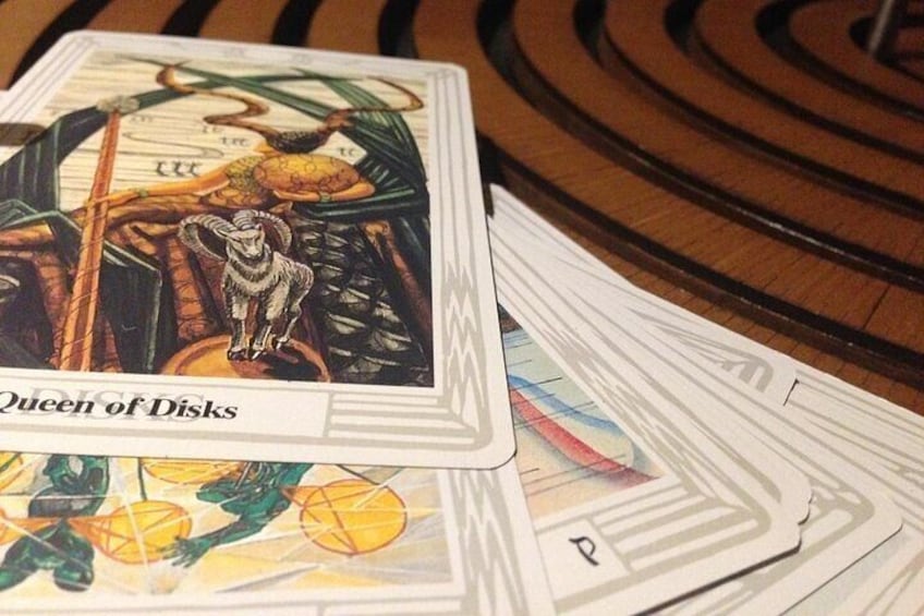 A tarot card titled 'Queen of Disks' with a goat and a ram on it, placed on a table with other cards. 3