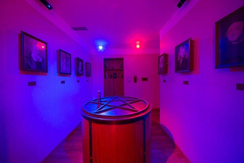 Un couloir avec une table ronde, des tableaux encadrés accrochés aux murs et une porte au fond. 5