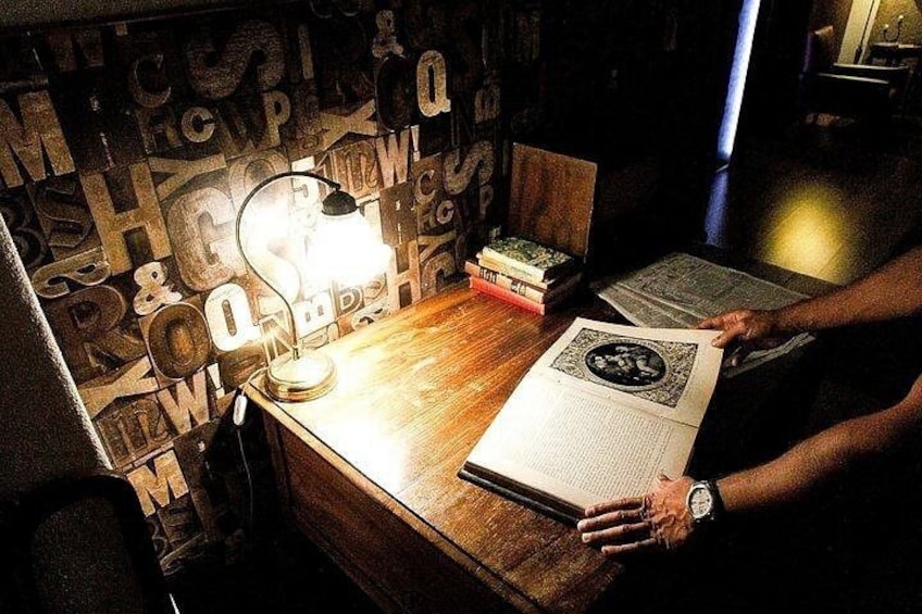 A person reading a book at a wooden table with a lamp, surrounded by books and papers. 4
