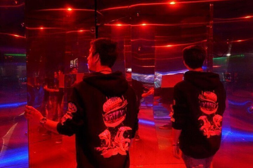 Dos personas con sudaderas con un diseño gráfico, de pie en una habitación con iluminación roja y superficies reflectantes. 5